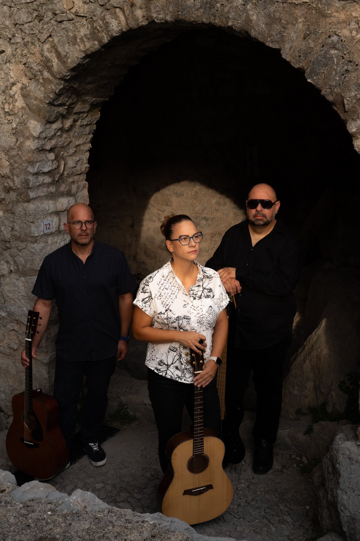 Troje članova Coffee Shop Acoustica s gitarama u kamenom prolazu.